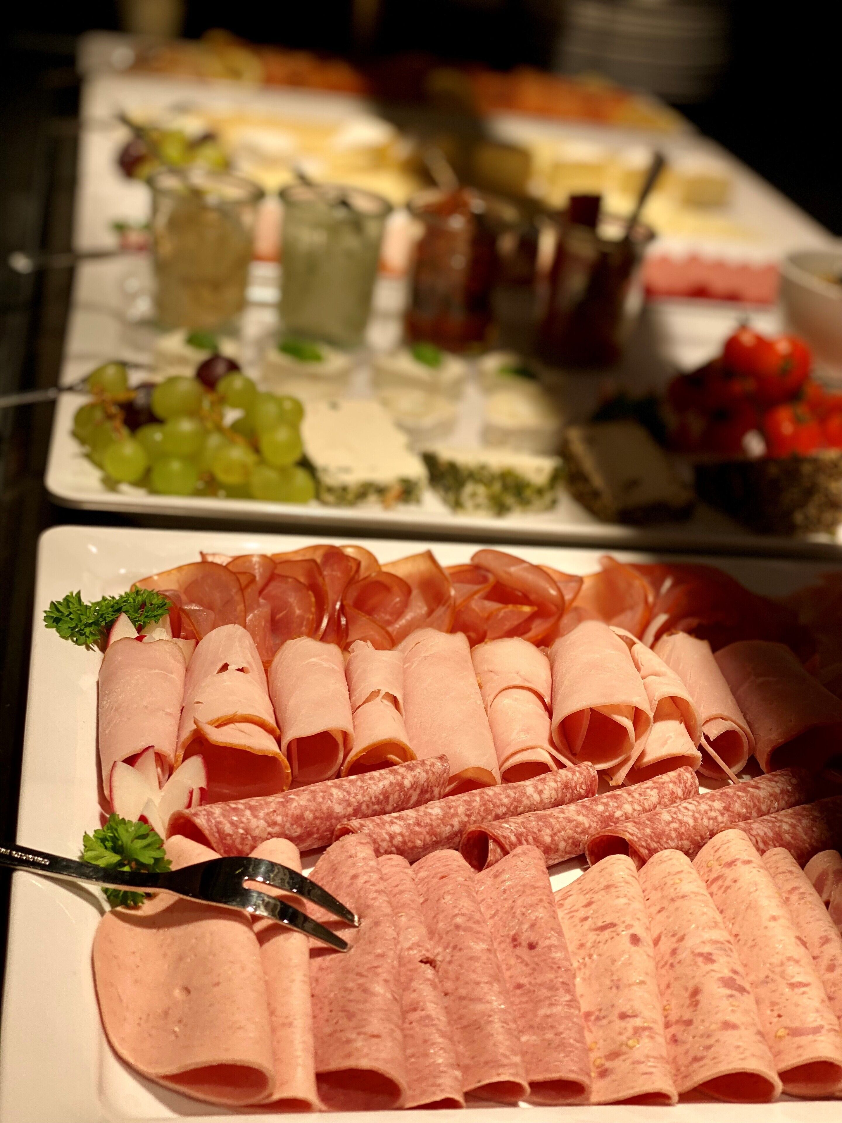 Un bufé con diversas opciones de comida, incluyendo fiambres, quesos y frutas.