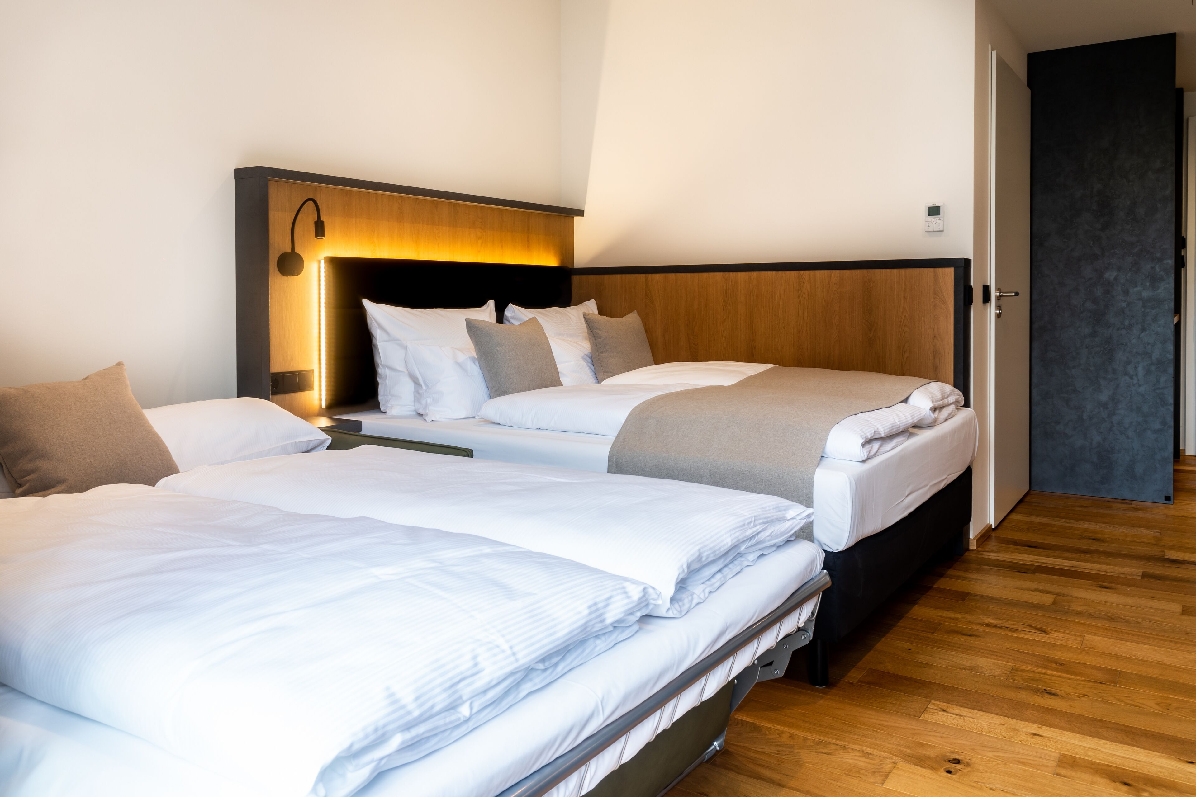 Habitación de hotel con dos camas, cabecero de madera, mesita de noche y una puerta a la derecha.