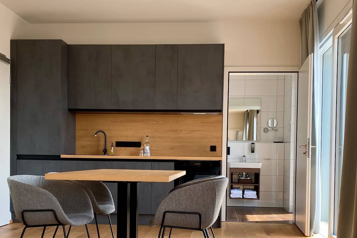 Une cuisine moderne avec des meubles de couleur sombre, un plan de travail en bois et un coin repas comprenant une table et des chaises.