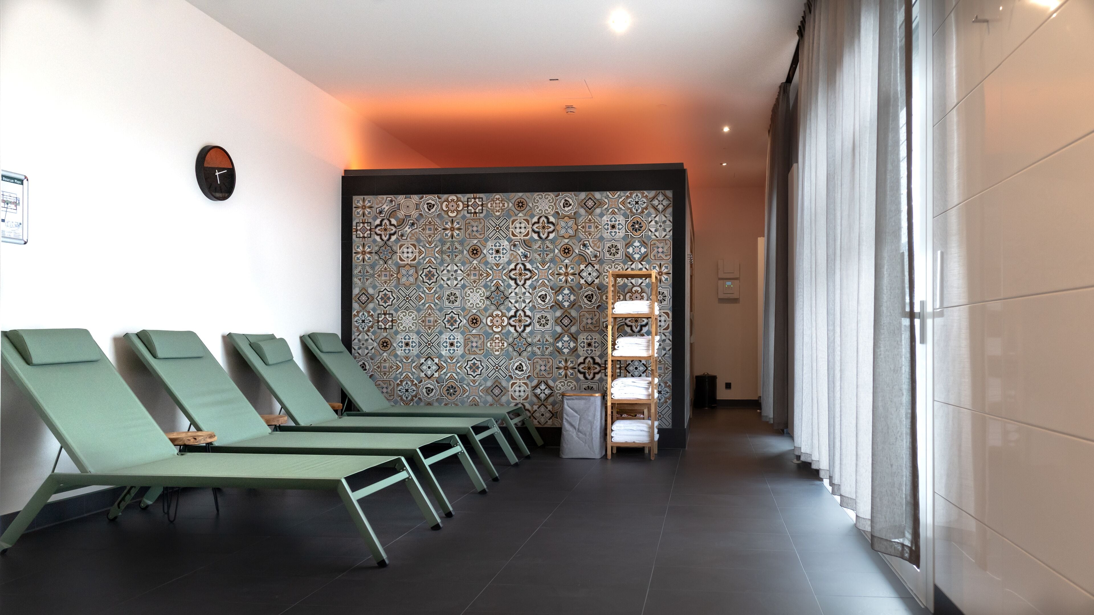 A spa area with green lounge chairs, a patterned wall, and a hallway leading to a room with a large window.