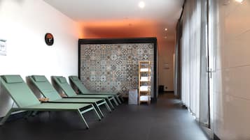 A spa area with green lounge chairs, a patterned wall, and a hallway leading to a room with a large window.