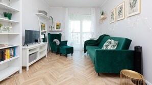 Una sala de estar moderna con un sofá verde, un mueble de entretenimiento blanco y un suelo de madera con patrón de espiga.