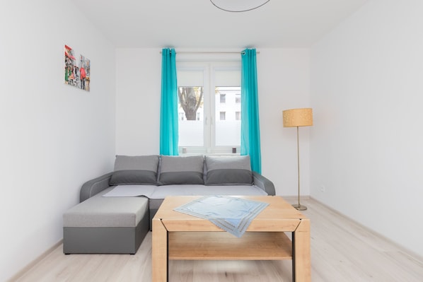 A modern living room with a grey sofa, teal curtains, a wooden coffee table, and a floor lamp.
