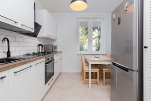 A modern kitchen with white cabinets, a stainless steel refrigerator, a wooden countertop, and a window with a view of greenery.