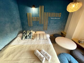 A modern hotel room with a bed, pillows, a bedside table, a round table, and a wall with vertical wooden slats. - Hostel Have a nice Day HVNI (Odawara)