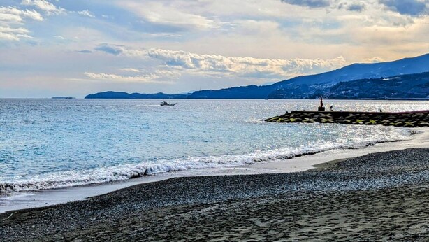 A beach with a rocky shoreline, calm sea, and distant mountains.