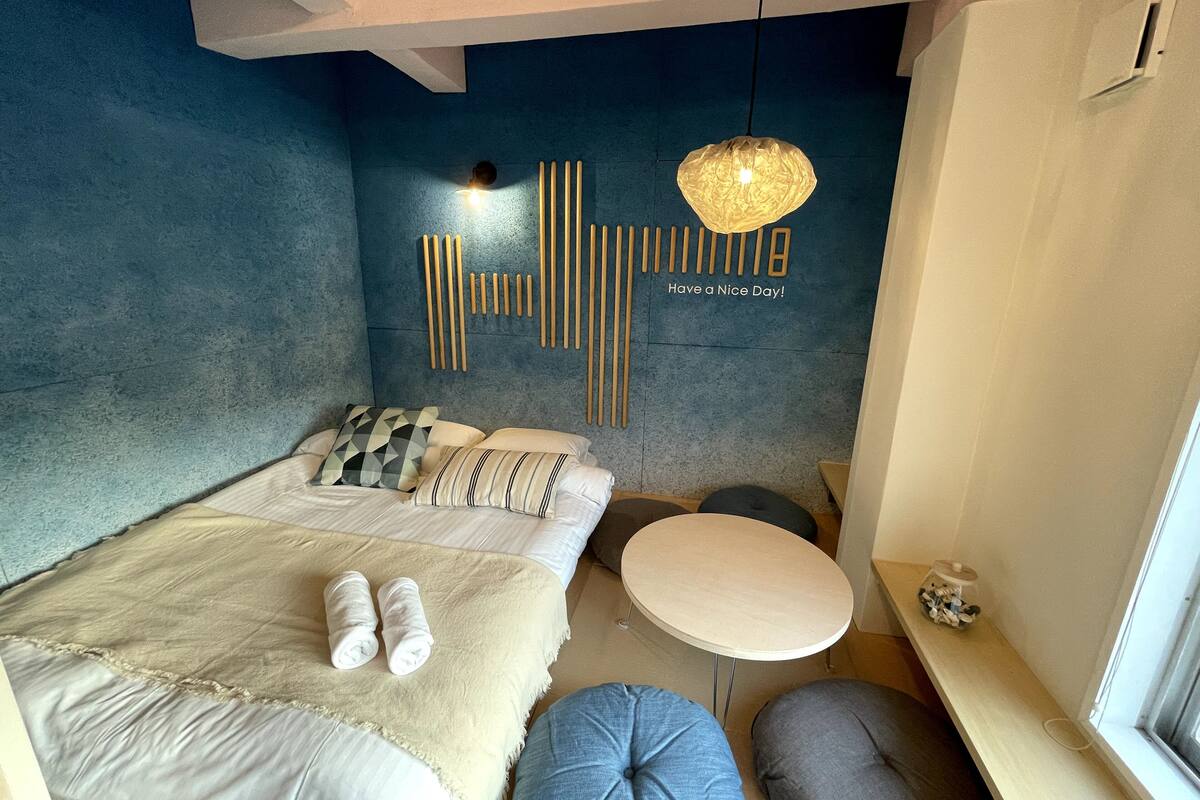 Um quarto moderno com cama, almofadas, uma mesa redonda e uma luminária fixada na parede.