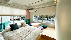 A modern bedroom with a large bed, a small round table, and a window with a view of the street.