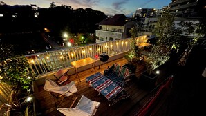 A rooftop terrace with wooden flooring, multiple seating areas, and string lights.