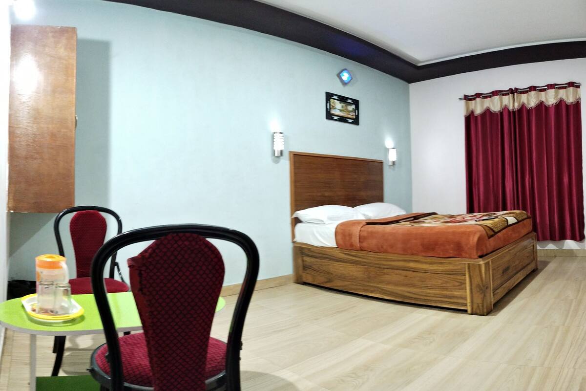 Een hotelkamer met een bed, een stoel, een tafel met een fles en een wandlamp.