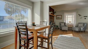 Un comedor con mesa y sillas de madera, una chimenea y una zona de estar con sillones y otomanas.