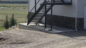 A building with a white exterior and a black metal staircase leading to a door. - Golden Views In Every Direction! (Ennis)