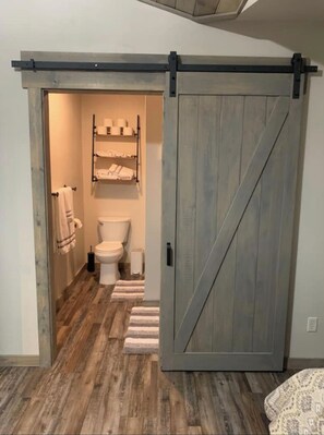 A bathroom with a toilet, towel rack, and a wooden floor. - Golden Views In Every Direction! (Ennis)