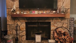 A living room with a stone fireplace, a mounted flat-screen TV, and a modern chandelier.