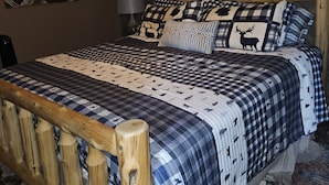A bedroom with a wooden bed frame, a checkered bedspread, and a ceiling fan.