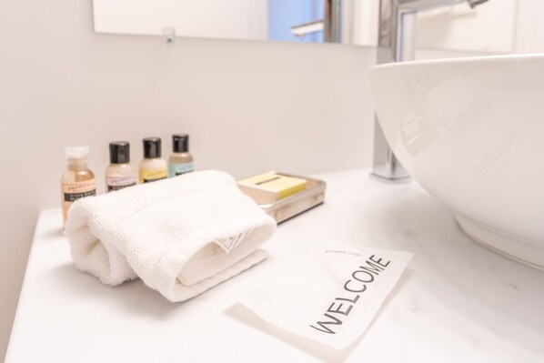 A bathroom vanity with a white sink, a folded white towel, and a welcome card.