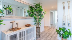 A modern hallway with a wooden console table, a large mirror, a potted bamboo plant, and two decorative bat-shaped wall art pieces. - Spacious condo with beautiful water views | WIFI 100+ Mbps (Sunny Isles Beach)