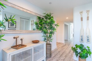 Un pasillo moderno con una consola de madera, un espejo grande, una planta de bambú en maceta y dos piezas decorativas de arte mural con forma de murciélago.