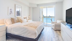 A bedroom with a large bed, a TV, a chair, and a view of the water. - Spacious condo with beautiful water views | WIFI 100+ Mbps (Sunny Isles Beach)