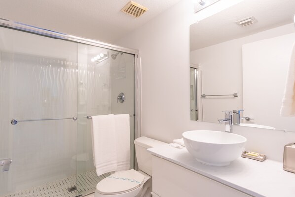 Een moderne badkamer met een douchecabine van glas, een wit toilet en een grote witte wastafel met een waskom.