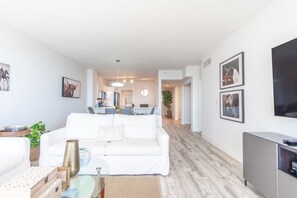 A modern living room with a white sofa, a glass coffee table, and a flat-screen TV on a stand.