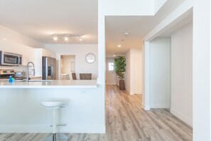 Una cocina moderna con armarios blancos, electrodomésticos de acero inoxidable y una isla central con taburetes de bar.