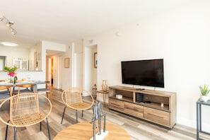 A modern living room with a flat-screen TV, wooden furniture, and a dining area with a table and chairs.