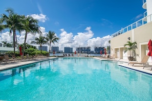 A swimming pool with lounge chairs and palm trees, overlooking a cityscape with buildings and construction cranes.