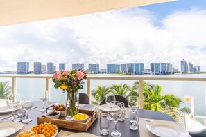 A dining table set with plates, glasses, and a waffle, overlooking a city skyline and water. - Modern condo with amazing intracoastal views (Sunny Isles Beach)