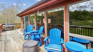 Une terrasse couverte avec des fauteuils Adirondack bleus, un barbecue et une table ronde.