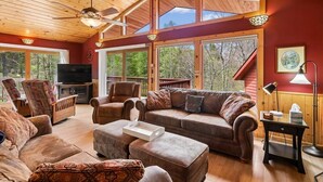 Un salon spacieux avec un plafond en bois, de grandes fenêtres, un téléviseur et des sièges confortables.
