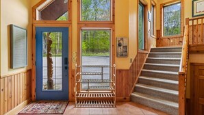 Un intérieur en bois avec une porte bleue, un escalier et une vue sur l’extérieur.