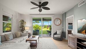 Ein modernes Wohnzimmer mit großem Fenster, Deckenventilator, Sofa, Couchtisch und Fernseher.