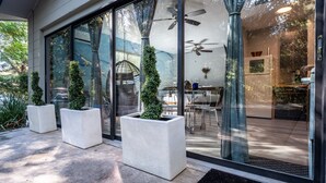 Ein moderner Hauseingang mit großen Glasüren, Topfpflanzen, Deckenventilatoren und einem sichtbaren Küchenbereich mit Kühlschrank und Esstisch.