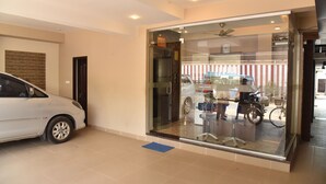 A modern hotel entrance with a glass door, a white car parked inside, and a motorcycle outside. - Kommiya Inn (Kumbakonam)