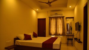 A bedroom with a bed, a chair, a desk, and a television. - Kommiya Inn (Kumbakonam)