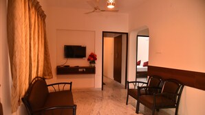 A hotel room with a TV mounted on the wall, a desk with a vase of flowers, and two chairs. - Kommiya Inn (Kumbakonam)