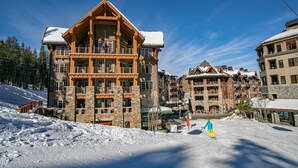 A multi-story lodge with stone and wood construction, ski slopes, and a clear blue sky. - Luxury Studio In The Village At Northstar - Big Horn 405 (Truckee)