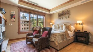 A bedroom with a large window, two wicker chairs, a bed with patterned bedding, a nightstand, and a wall-mounted lamp. - Luxury Studio In The Village At Northstar - Big Horn 405 (Truckee)