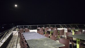 An outdoor dining area with tables and chairs, a railing, and a view of the night sky. - Hotel Vijay Krishna (Madurai)