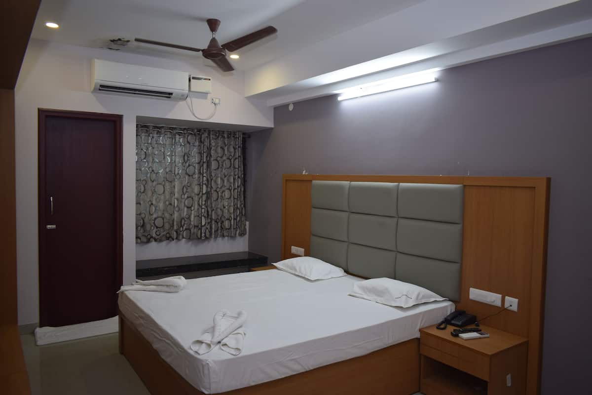 A bedroom with a large bed, a wooden headboard, a bedside table with a phone and remote, and an air conditioning unit on the wall.