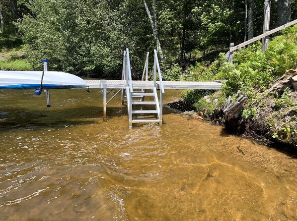 A wooden bridge over a clear stream with a ladder leading to a dock.