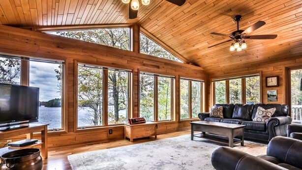 A spacious living room with large windows, a leather sofa, a coffee table, and a television. - Gorgeous Private Home with magnificent lake views! Great Firepit to watch the Su (Harshaw)