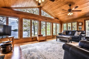 A spacious living room with large windows, a leather sofa, a coffee table, and a television.