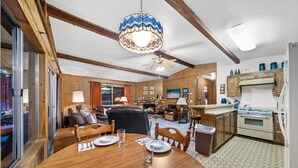 A dining area with a wooden table set for four, a ceiling fan, and a kitchen area with wooden cabinets and a stove.