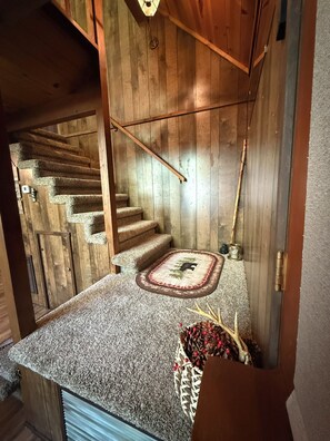 A wooden staircase with a carpeted landing and a decorative pine cone arrangement.