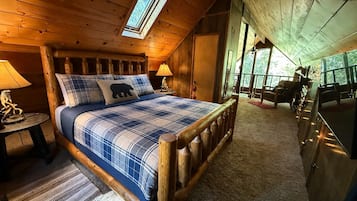 Ein Schlafzimmer einer Holzhütte mit einem Bett, zwei Nachttischlampen, einem Fenster und Blick ins Freie.