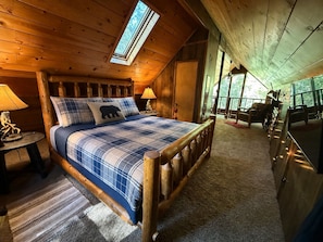 A wooden cabin bedroom with a bed, two bedside lamps, a window, and a view of the outdoors.