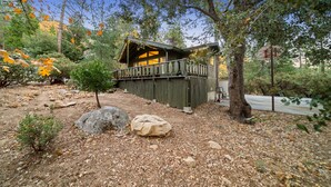 A rustic cabin with a porch, surrounded by trees and rocks.