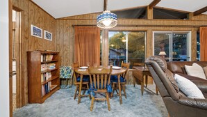 A cozy living room with a wooden dining table, chairs, a leather sofa, and a bookshelf.